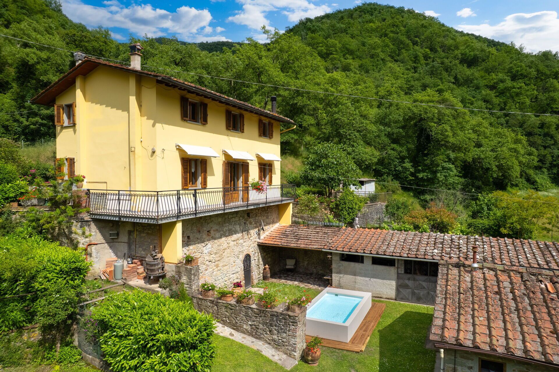 Una villa amarilla con base de piedra, piscina y jardín.