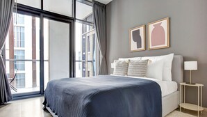 Un dormitorio moderno con una cama grande, una mesita de noche, una lámpara y dos cuadros en la pared.