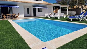 Une piscine avec des chaises longues, une table de patio et un espace abrité avec des parasols.