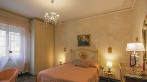 A bedroom with a bed, a chandelier, a painting, a lamp, and a dresser. - Butterfly Apartment In Lucca (Lucca)