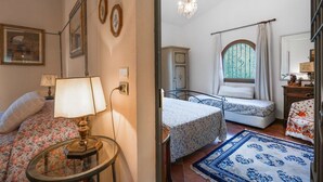 Une chambre avec deux lits, un lustre, une fenêtre avec des rideaux et un tapis à motifs floraux.