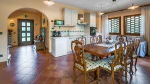 Een ruime keuken met een eethoek, met een centraal kookeiland, houten stoelen en een groot raam met uitzicht.