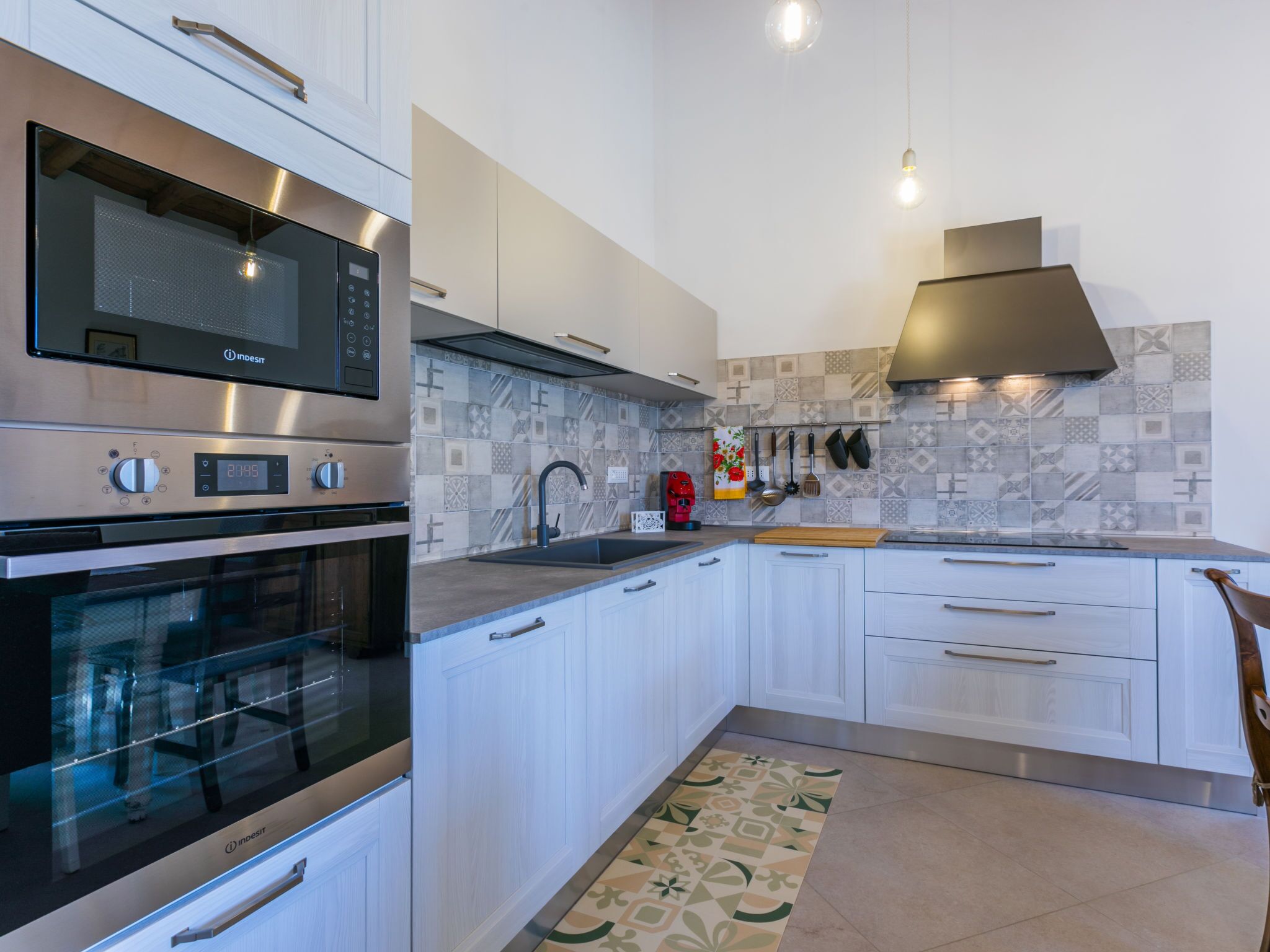 A modern kitchen with stainless steel appliances, white cabinetry, and patterned backsplash tiles.