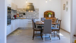 Une cuisine moderne avec des meubles blancs, une table à manger en bois et des luminaires suspendus.