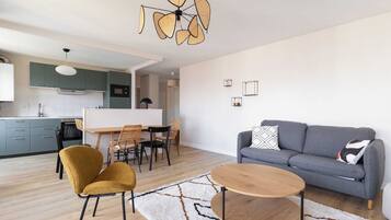 A modern living room with a grey sofa, mustard chairs, a wooden coffee table, and a dining area with a white table and chairs.