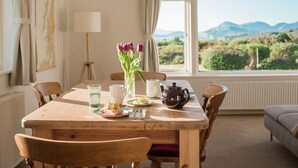 A dining area with a wooden table, chairs, and a view of the countryside through a window.