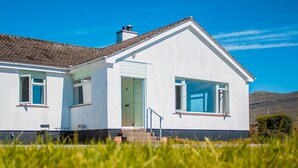 A single-story house with a white exterior, a brown tiled roof, and a clear blue sky in the background.