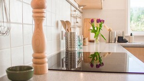 A modern kitchen with white tiled walls, stainless steel appliances, wooden utensils, and a green bowl on the counter.