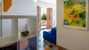 A modern interior with a blue sofa, a colorful abstract painting, and a kitchen area with a bowl on the counter.