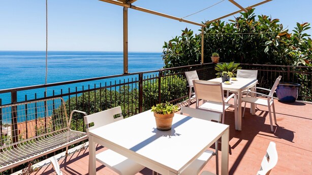 A terrace with a table and chairs, overlooking a coastal view.