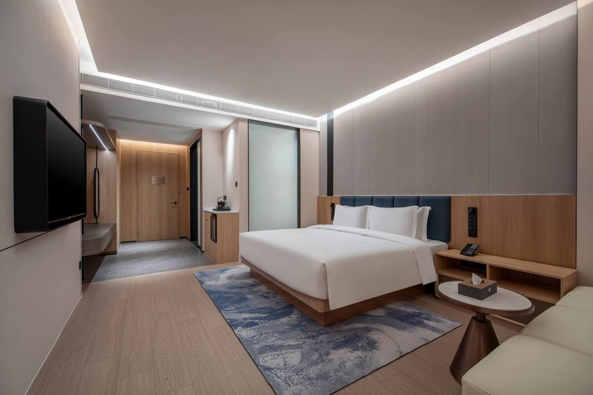 Ein modernes Hotelzimmer mit einem großen Bett, Nachttischen, einem Flachbildfernseher und einer kleinen Sitzecke.