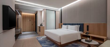 A modern hotel room with a large bed, bedside tables, a flat-screen TV, and a small seating area.