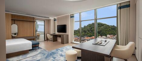 A modern hotel room with a bed, a desk, a TV, and a view of a cityscape.
