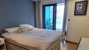 A bedroom with a bed, a desk, a chair, a window with curtains, and a view of the outside.