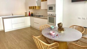 Une cuisine moderne avec des meubles blancs, un four à micro-ondes et une cuisinière. On y trouve également un coin repas avec une table ronde et des chaises en osier.