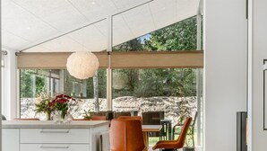 A modern kitchen with a large island, dining area with orange chairs, and a view of a rocky landscape through large windows. - "Zoya" -  from the sea by Interhome (Hals)