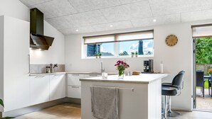 A modern kitchen with white cabinetry, a central island, and a window overlooking a garden. - "Zoya" -  from the sea by Interhome (Hals)