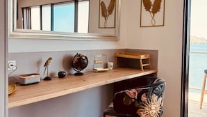 Une chambre moderne avec un plancher en bois, un grand miroir, un bureau agrémenté d’un globe terrestre et d’une sculpture d’oiseau, ainsi qu’une chaise à motifs floraux.