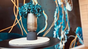 Une pièce moderne avec une table ronde, un vase rempli de fleurs bleues et un grand tableau abstrait accroché au mur.
