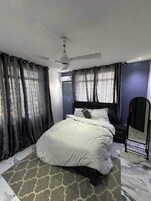A bedroom with a bed, a ceiling fan, a mirror, and curtains.