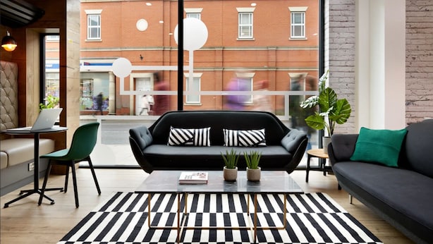 A modern living room with a black sofa, green chairs, and a striped rug. There is a laptop on a table and a potted plant. - For Students Only - Modern Rooms in Lincoln (Lincoln)