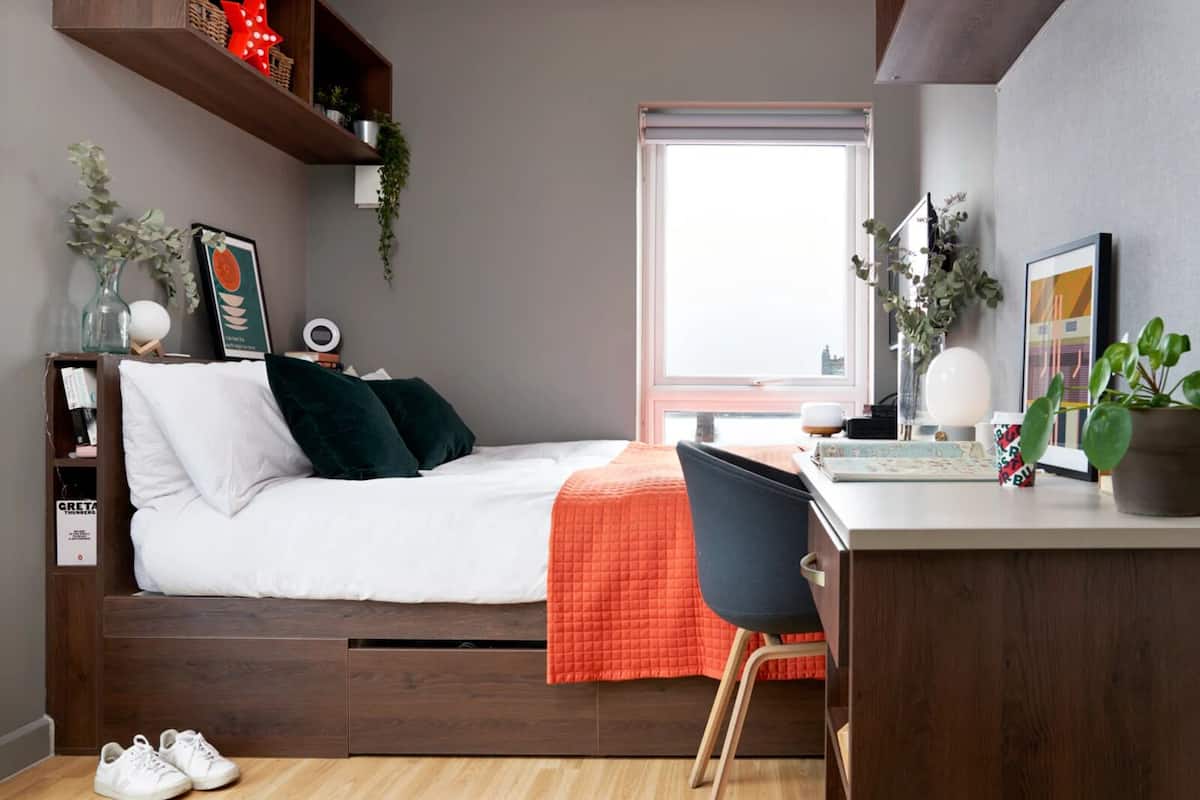 Un dormitorio con cama, escritorio y silla. Se ve una ventana con vistas al exterior.