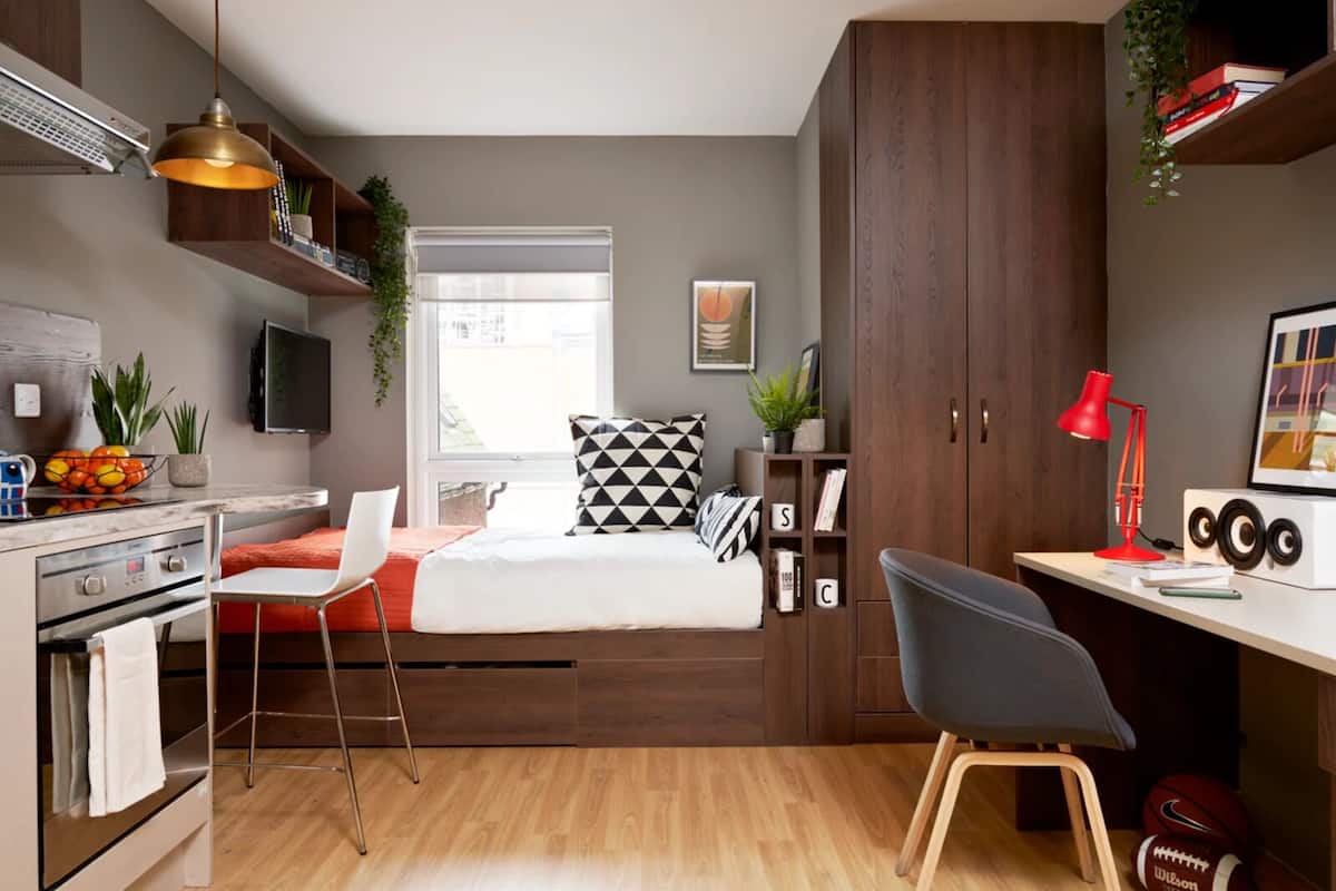 Un dormitorio pequeño con cama, escritorio, silla, televisor y armario.