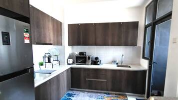A compact kitchen with dark wood cabinets, a stainless steel refrigerator, a microwave, and a sink.