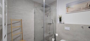 Ein modernes Badezimmer mit Duschkabine aus Glas, einer Holzleiter, einer Toilette und einem kleinen Regal mit einer Pflanze.