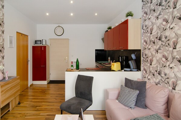 Un espacio habitable compacto con kitchenette, comedor y zona de estar con sofá y sillón.