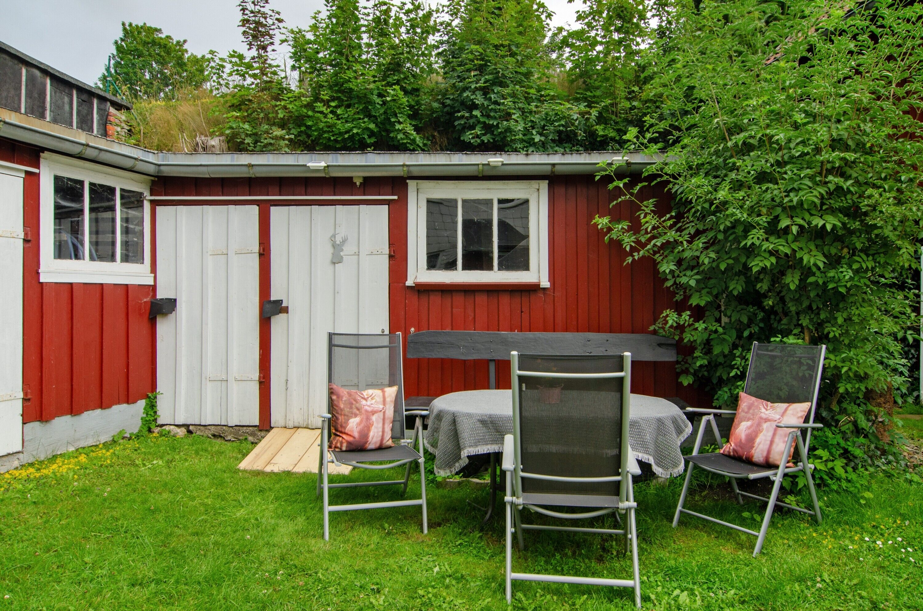 A red and white shed with a door and windows, a table with chairs, and a small garden area.