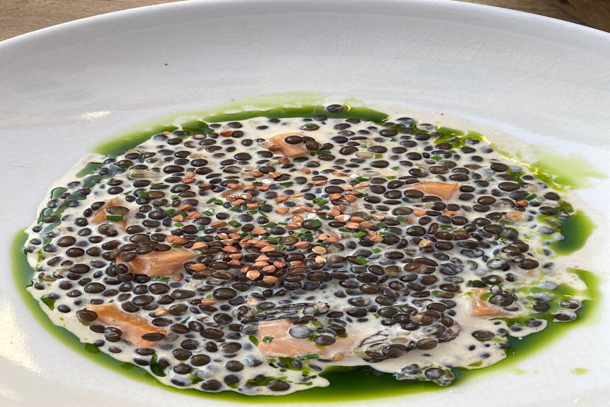 Un piatto con lenticchie nere, erbe verdi e salsa verde.
