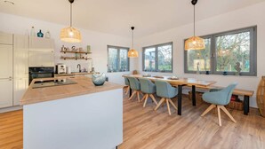 A modern kitchen with a central island, wooden flooring, and pendant lighting. - "Haffhus" Vacation Home with a Balcony, Terrace, and 2 Bathrooms - Modern Vacation Home (Usedom)