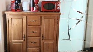 Een keuken met een rode magnetron, koffiezetapparaat en waterkoker op een houten kast.