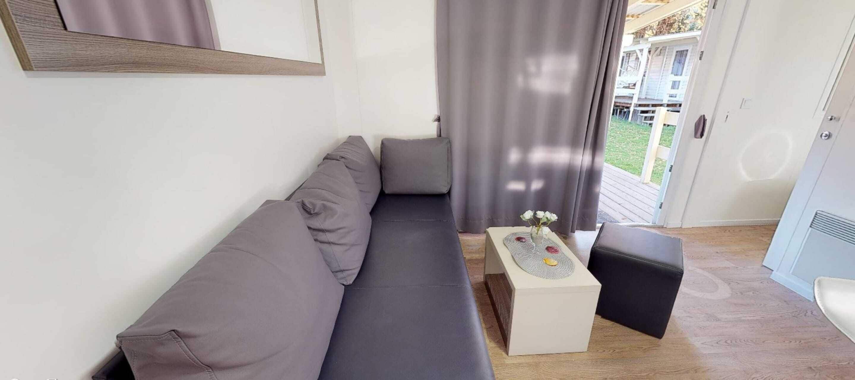 Una sala moderna con un sofá gris, una mesita de centro blanca con un florero, y un reposapiés negro.