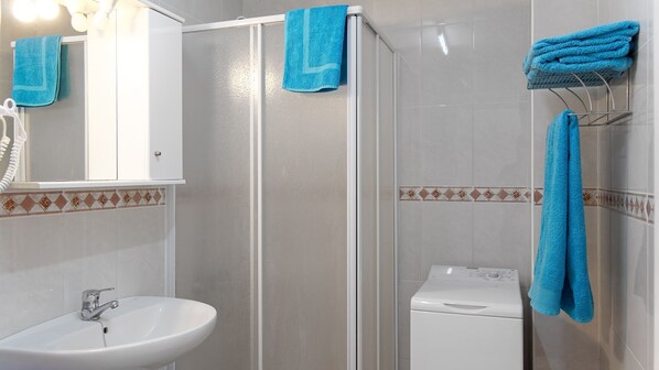 A bathroom with a shower, a sink, and a toilet. There are blue towels hanging on the wall and a towel rack. - LOMA ESTRELLA (Arguineguín)