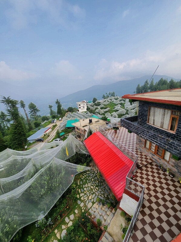 A residential area with a red-roofed building, a stone-paved courtyard, and a view of distant mountains.
