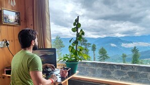 A person working at a wooden desk by a window with a view of mountains. - Talaighar Farmstay Shimla (Fagu)
