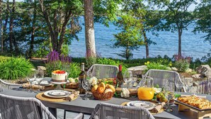 Un espace de restauration en plein air avec des chaises en osier, une table dressée avec des assiettes, des verres, un gâteau et un panier de pain.