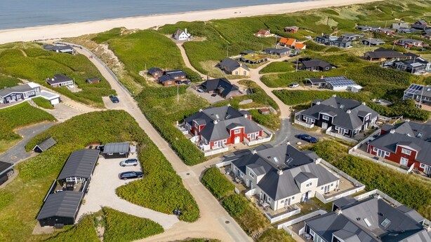 An aerial view of a coastal residential area with houses, roads, and a beach.