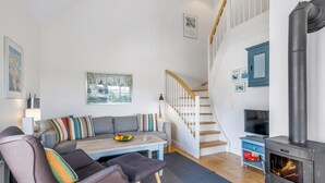 A cozy living room with a sofa, a dining table, a fireplace, and a staircase.