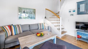 A modern living room with a grey sectional sofa, a wooden coffee table with fruit, a staircase with white railings, and a blue cabinet.