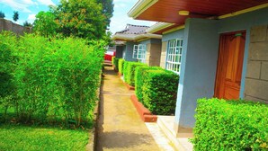 A pathway flanked by neatly trimmed hedges leading to a row of houses with blue walls and wooden doors. - Holiday Premier Hotel (Ol Kalou)