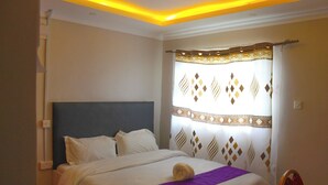 A hotel room with a bed, a headboard, a curtain with a geometric pattern, and a purple throw blanket. - Holiday Premier Hotel (Ol Kalou)
