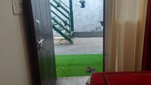 A room with a bed, a green mat, and a door leading to an outdoor area with a staircase. - Kaushik Cottage (Mussoorie)