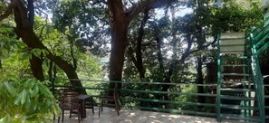 Un espacio al aire libre cubierto con una mesa y sillas de madera, rodeado de árboles y una barandilla de metal verde.