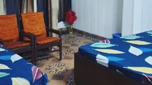 A room with two beds, a chair, and a table with a vase of flowers. - Kaushik Cottage (Mussoorie)