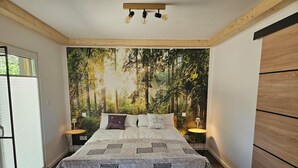 A bedroom with a large bed, a forest-themed wall mural, and a small round table with a lamp.