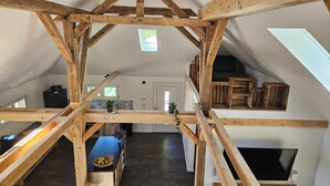A loft-style living space with exposed wooden beams, a kitchen area, and a dining table with a bowl of fruit.