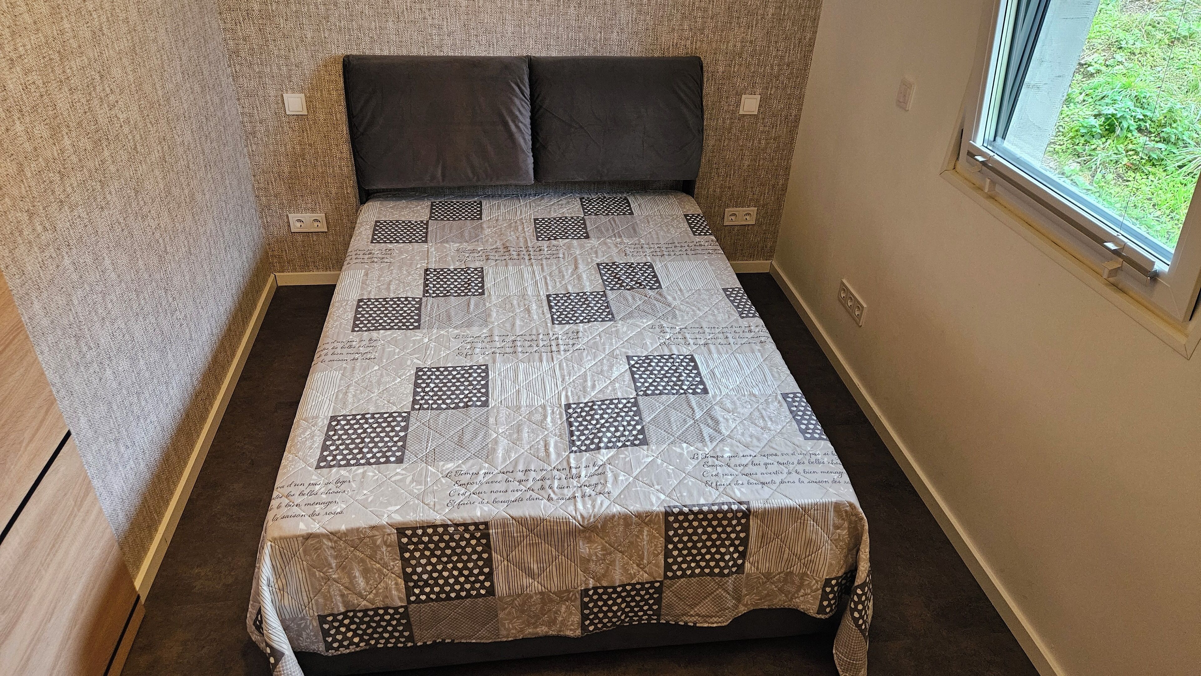 A bed with a quilt, a window, and a wall with a textured pattern.
